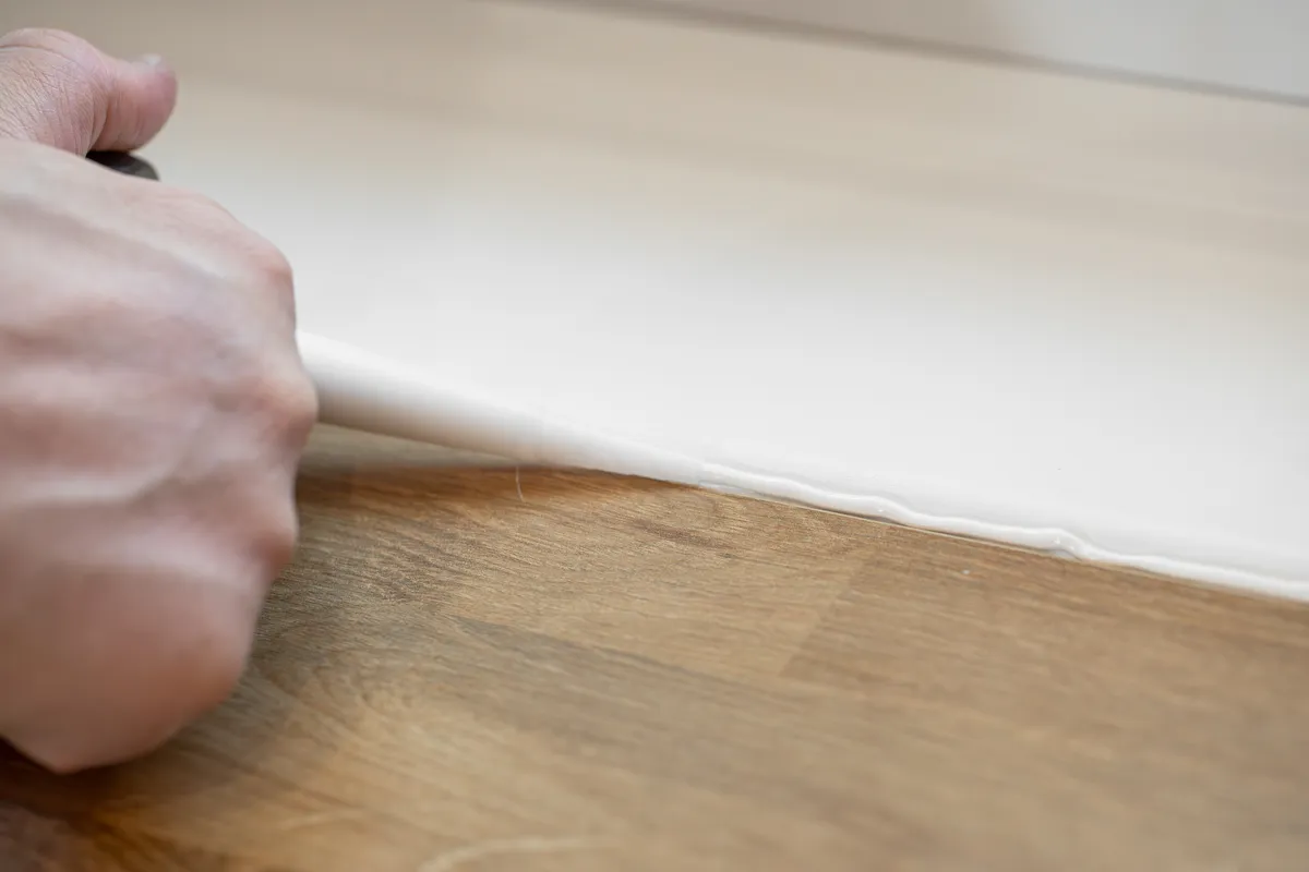 Hand brengt een witte kitnaad aan langs een houten vloer