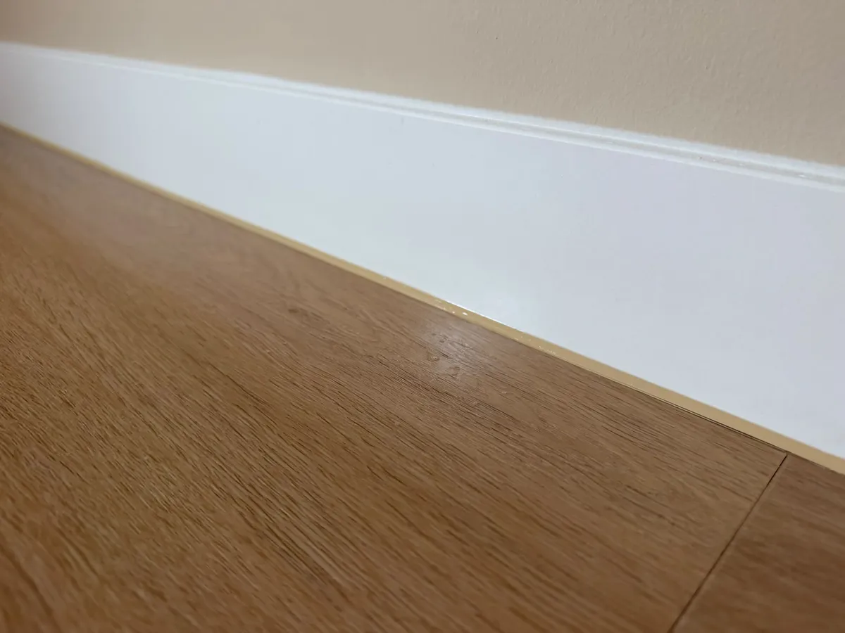 Detail van een strakke kitnaad tussen plint en houten vloer