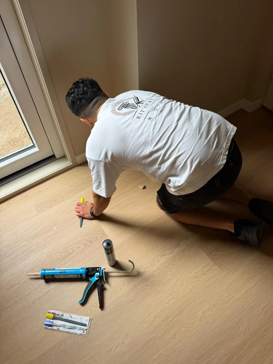 Vakman brengt kit aan langs plinten bij een houten vloer